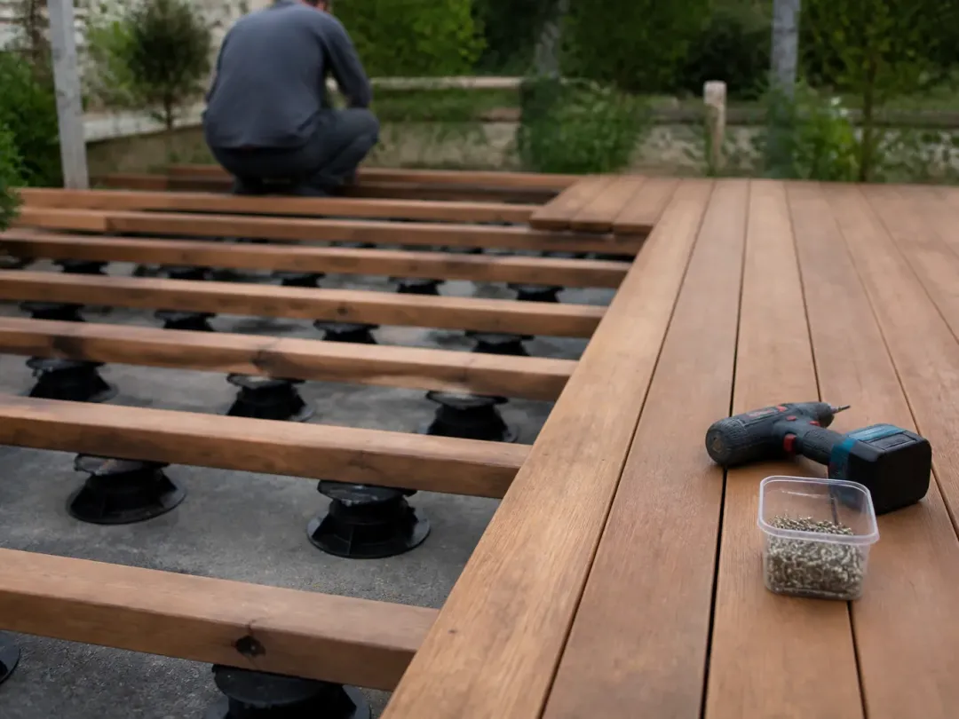 Terrasse en bois en cours de pose sur lambourdes et plots réglables, visseuse posée sur les lames
