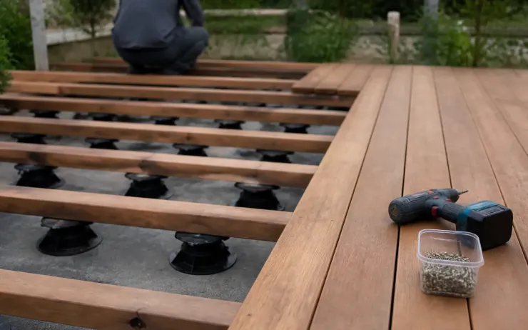 Terrasse en bois en cours de pose sur lambourdes et plots réglables, visseuse posée sur les lames