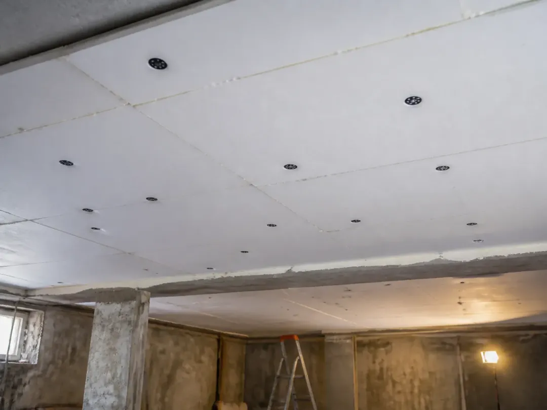 Plafond d’un sous-sol recouvert de panneaux isolants blancs fixés par des chevilles à rosace