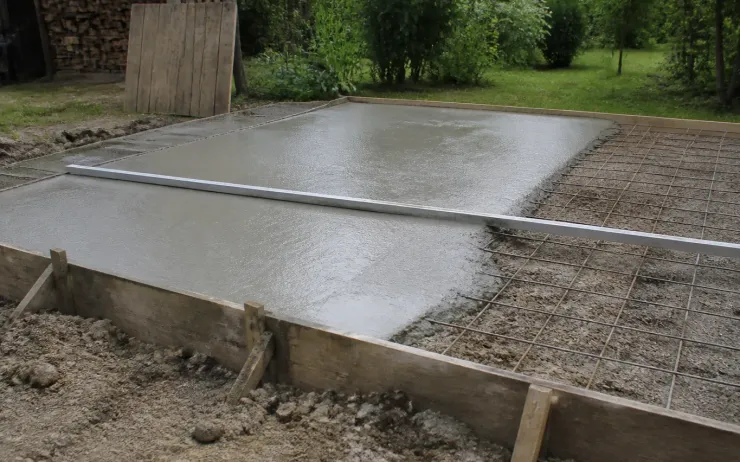 Dalle de béton fraîchement coulée dans un coffrage en planches, treillis soudé encore visible sur la partie non coulée