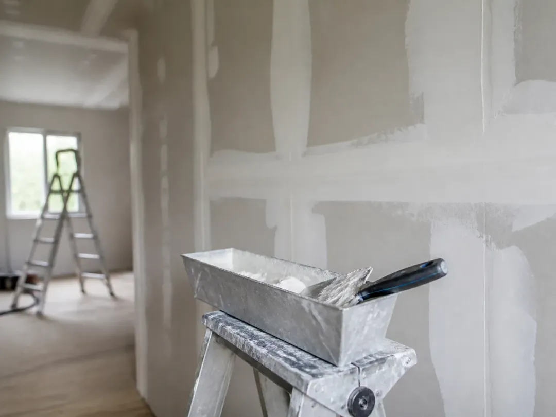 Mur en plaques de plâtre aux joints enduits, auge et couteau à enduire posés sur un escabeau
