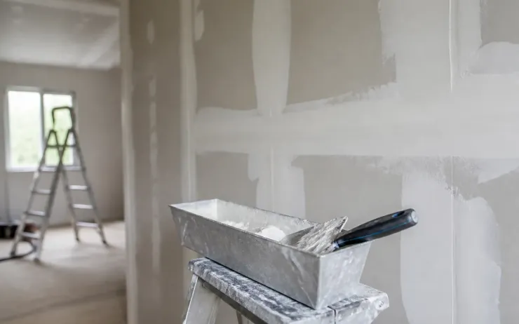 Mur en plaques de plâtre aux joints enduits, auge et couteau à enduire posés sur un escabeau