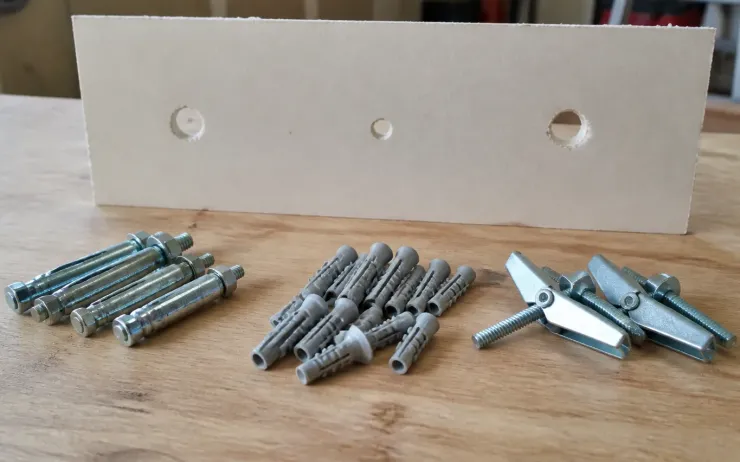 Chevilles métalliques à expansion, chevilles plastiques et chevilles à bascule alignées devant une chute de plaque de plâtre percée