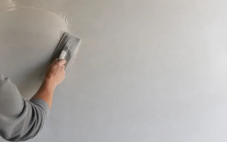 Main étalant une fine couche d’enduit blanc sur un mur avec une lisseuse inox