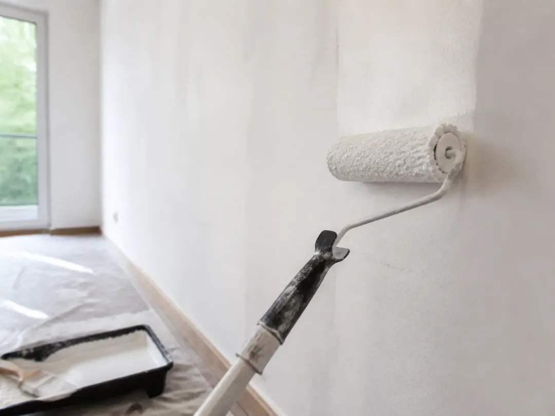 Rouleau chargé de peinture blanche sur un mur, bac à peinture posé sur une bâche