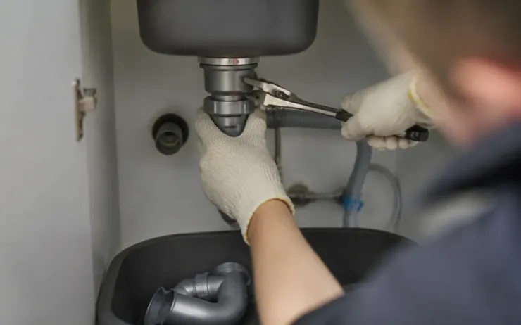 Mains gantées desserrant l’écrou d’un siphon sous un évier avec une clé à molette