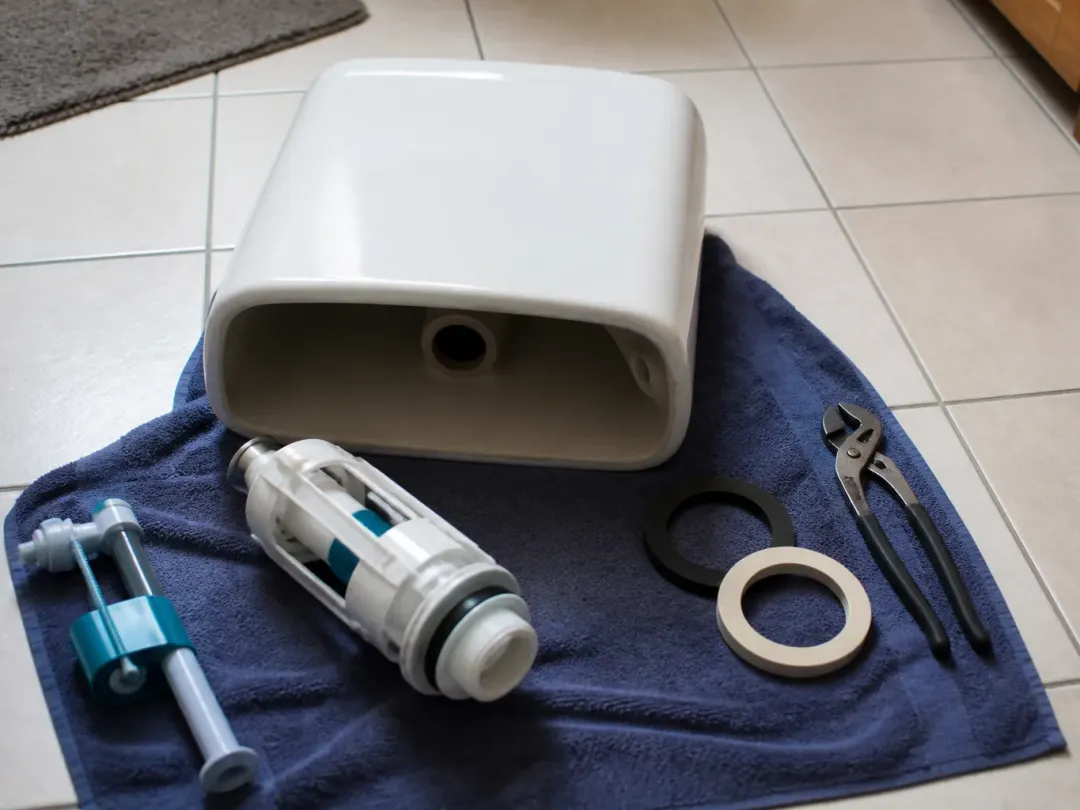 Couvercle de réservoir de WC posé sur une serviette avec un mécanisme de chasse neuf, un robinet flotteur, des joints et une pince