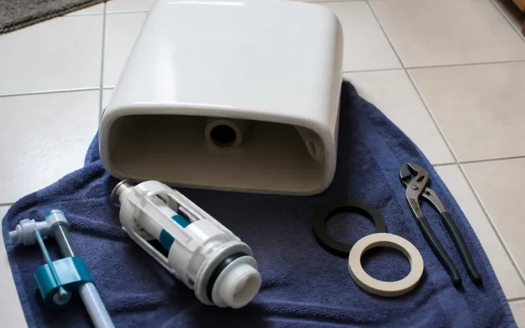 Couvercle de réservoir de WC posé sur une serviette avec un mécanisme de chasse neuf, un robinet flotteur, des joints et une pince