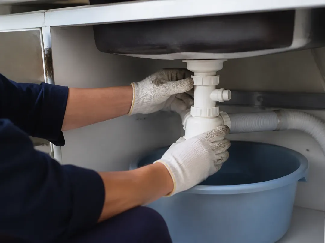 Mains gantées dévissant le siphon d'un évier au-dessus d'une bassine