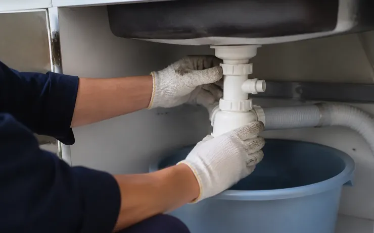 Mains gantées dévissant le siphon d'un évier au-dessus d'une bassine