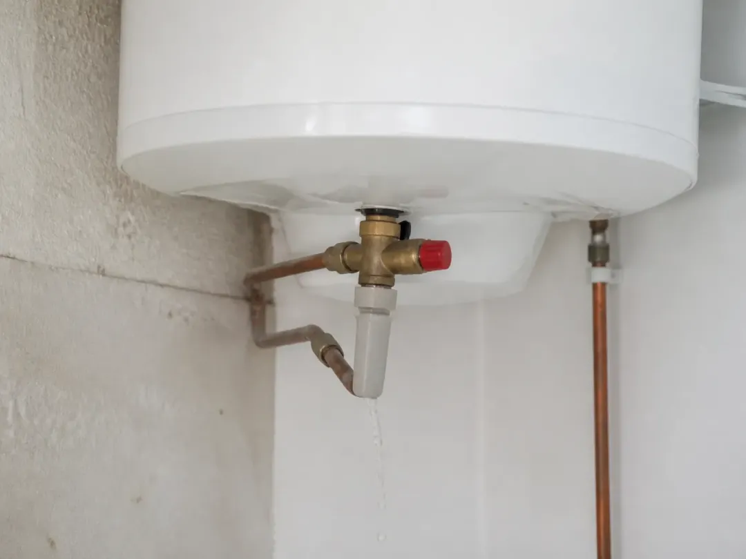 Bas d’un chauffe-eau électrique mural avec son groupe de sécurité en laiton et un filet d’eau à l’évacuation