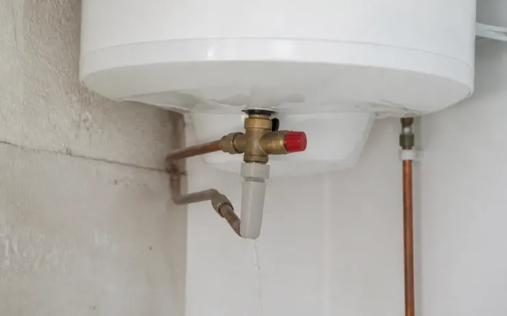 Bas d’un chauffe-eau électrique mural avec son groupe de sécurité en laiton et un filet d’eau à l’évacuation