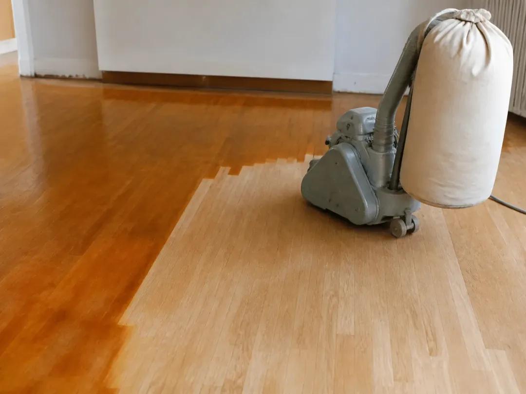 Ponceuse à parquet sur un sol en chêne dont une moitié est poncée et l’autre encore vernie