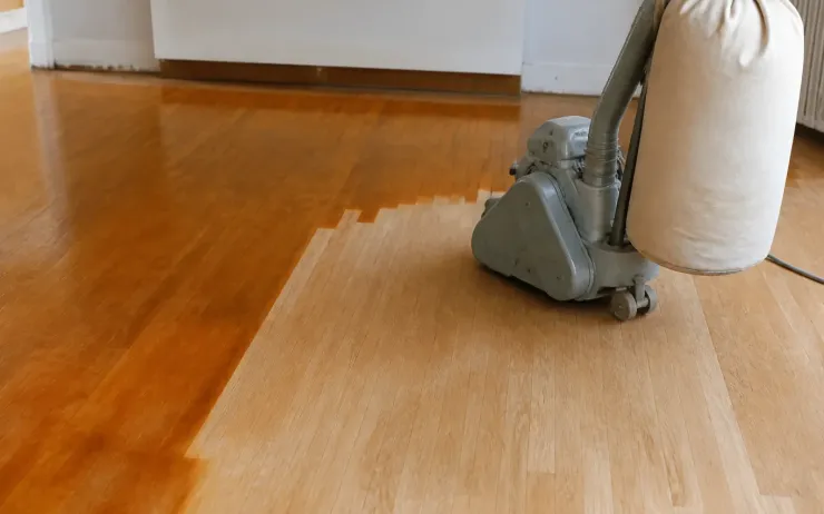 Ponceuse à parquet sur un sol en chêne dont une moitié est poncée et l’autre encore vernie