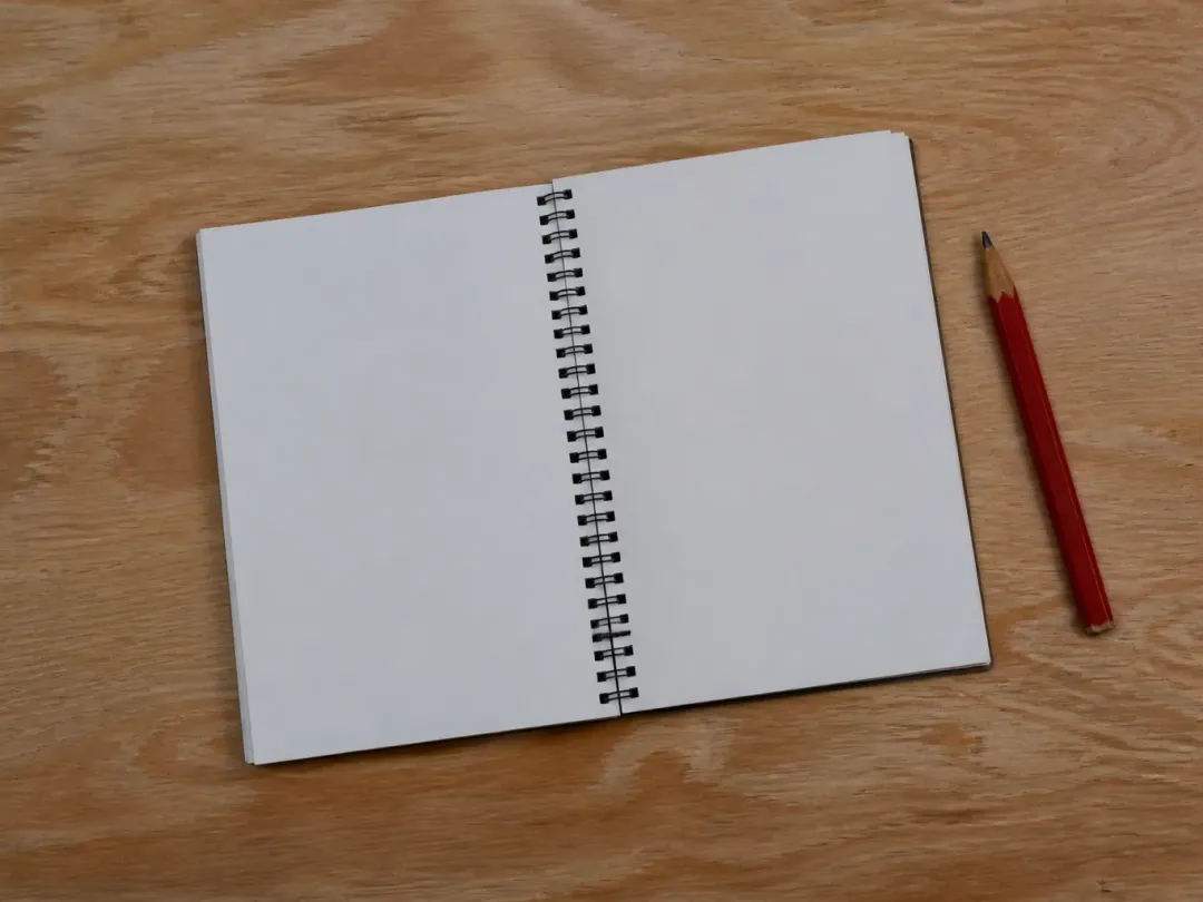 Carnet à spirale ouvert et crayon rouge posés sur une planche de contreplaqué