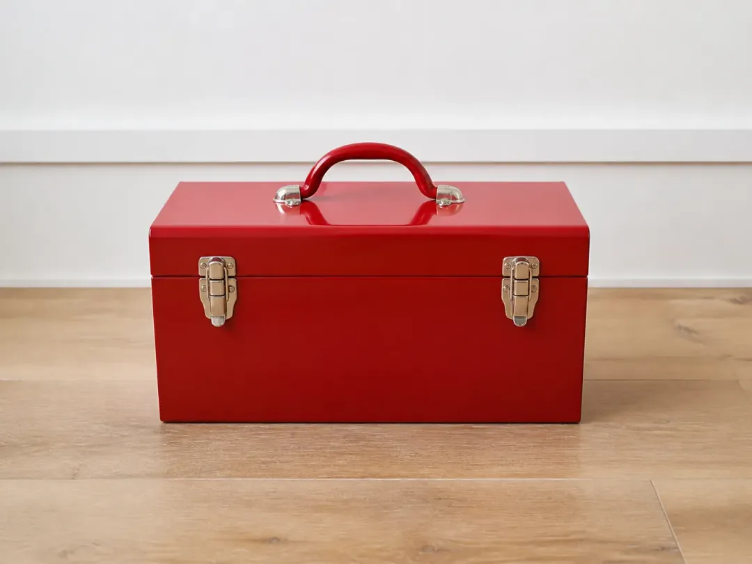Boîte à outils métallique rouge fermée, posée sur un plancher en bois clair