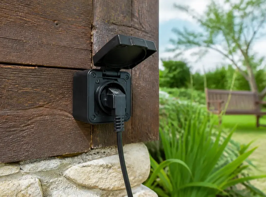 Prise pour extérieur murale avec câble branché près d'un jardin verdoyant