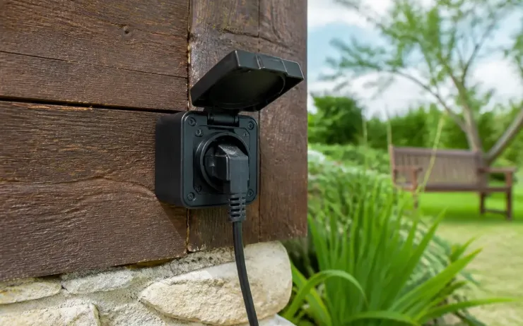 Prise pour extérieur murale avec câble branché près d'un jardin verdoyant